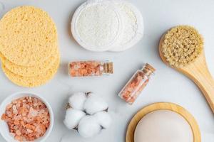 personal hygiene tools and cosmetics on white background. Face soap, brush with natural bristle. pink himalayan salt in a bowla, cotton and lufa reusable sponges for skin cleanser. photo