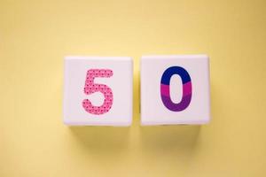 Close-up photo of a white plastic cubes with a colorful number 50 on a yellow background. Object in the center of the photo