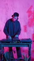 DJ moderno de aparência asiática executa uma faixa de música em iluminação neon. trabalhando no mixer, um homem coloca discos, trilhas sonoras, sons individuais e faz uma mixagem deles. vídeo vertical video