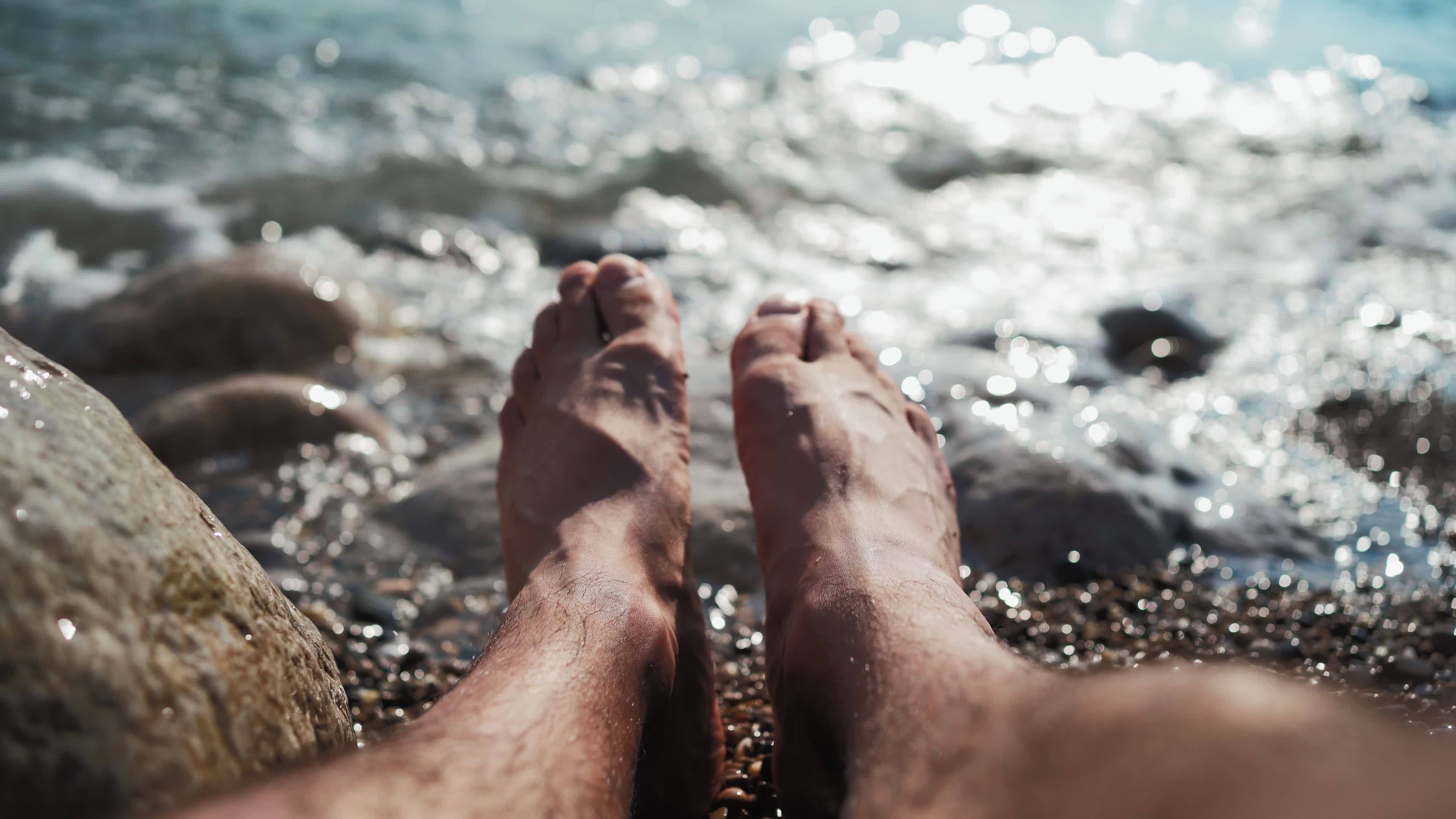 Close-up on the legs of an unrecognizable man relaxing on the sea beach on  a summer sunny day. Vacation and travel concept. From the first person. POV  13007630 Stock Video at Vecteezy