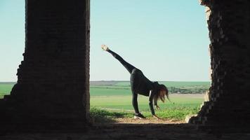 Beautiful athletic girl gymnast with a steep stretching becomes splits on the background scenery green fields. Slow motion. Shooting on the Steadicam video
