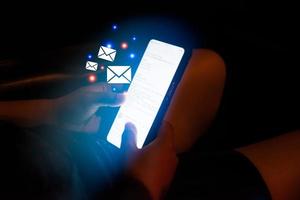 mano de mujer sosteniendo un teléfono revisando la pantalla virtual del icono de correo electrónico en el automóvil por la noche. concepto de negocio de mensaje de aplicación de conexión de tecnología digital. foto