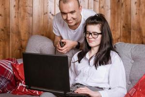 A young couple at home sitting on the couch communicating online via laptop with relatives photo