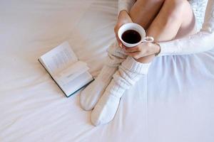 Lazy time in bed. Young woman in knitted knee socks on a white sheet reading photo