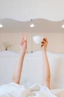 Young woman with a coffee mug in bed with white linens. Minimal happy morning photo