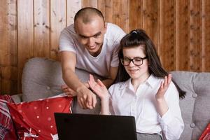 A young couple at home sitting on the couch communicating online via laptop with relatives photo