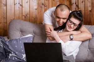 A young couple at home sitting on the couch communicating online via laptop with relatives photo