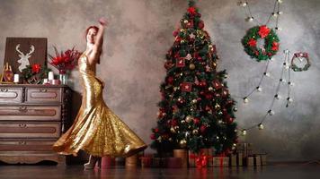 un' bellissimo donna nel un' d'oro sera vestito gira e balli vicino un' Natale albero decorato con nuovo anni giocattoli. festivo umore. alto qualità 4k metraggio video