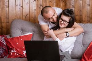 A young couple at home sitting on the couch communicating online via laptop with relatives photo