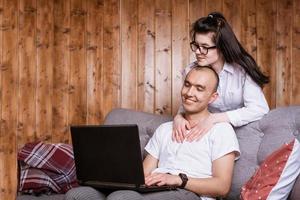 una pareja joven en casa sentada en el sofá comunicándose en línea a través de una laptop con parientes foto
