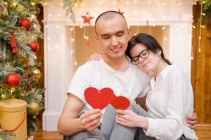 Couple in love, man and woman in white t-shirts, holding wooden red hearts photo