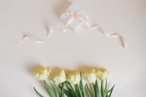 Spring yellow tulips and a gift box with a delicate peach bow and ribbon on a beige light background. Flat lay photo