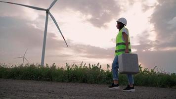 vrouw professioneel ecologie specialist in uniform met speciaal uitrusting in hand- gaat naar onderhoud een windmolen. alternatief en hernieuwbaar energie. modern technologie. groen elektriciteit concept. video