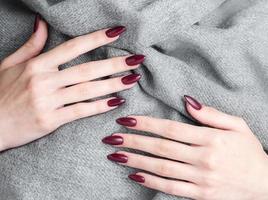 manos de una mujer joven con manicura roja oscura en las uñas foto