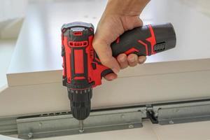 man assembling white table furniture at home using cordless screwdriver photo