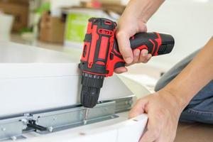 man assembling white table furniture at home using cordless screwdriver photo