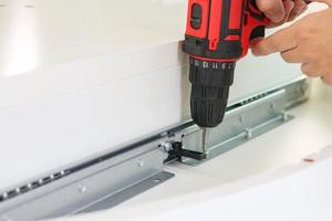 man assembling white table furniture at home using cordless screwdriver photo