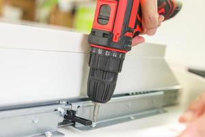 man assembling white table furniture at home using cordless screwdriver photo
