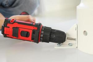 man assembling white table furniture at home using cordless screwdriver photo