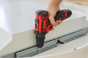 man assembling white table furniture at home using cordless screwdriver photo