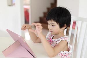 Little asian girl playing digital tablet at home photo