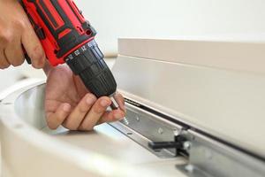 man assembling white table furniture at home using cordless screwdriver photo