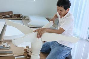 Asian man assembling white table furniture at home photo