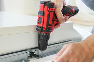 man assembling white table furniture at home using cordless screwdriver photo