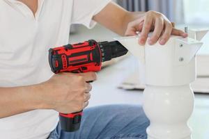 man assembling white table furniture at home using cordless screwdriver photo