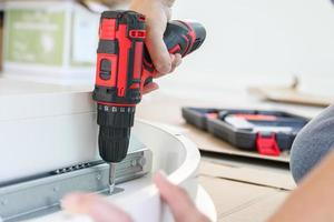 man assembling white table furniture at home using cordless screwdriver photo