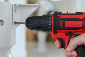 man assembling white table furniture at home using cordless screwdriver photo