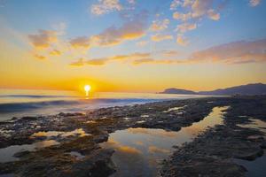 vista de una costa rocosa al atardecer. puesta de sol paisaje de rocas marinas en tiro de larga exposición foto