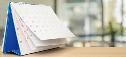 calendario de escritorio de papel blanco sobre una mesa de madera con una cita de fondo borrosa y concepto de reunión de negocios foto