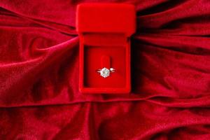 Diamond ring in jewelry gift box on red fabric background photo