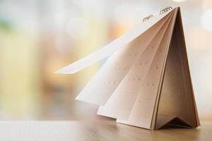 white paper desk calendar on wood table with blurred bokeh background appointment and business meeting concept photo