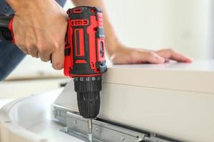 man assembling white table furniture at home using cordless screwdriver photo