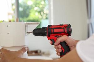 man assembling white table furniture at home using cordless screwdriver photo