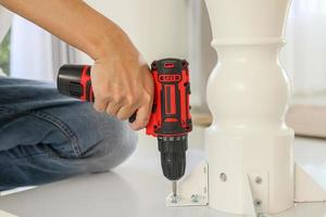 man assembling white table furniture at home using cordless screwdriver photo