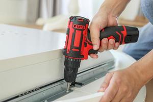 man assembling white table furniture at home using cordless screwdriver photo