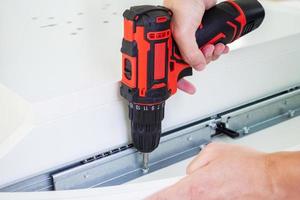 man assembling white table furniture at home using cordless screwdriver photo