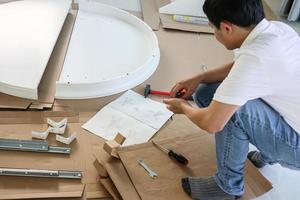 Asian man assembling white table furniture at home photo