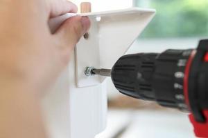 man assembling white table furniture at home using cordless screwdriver photo