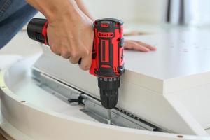 man assembling white table furniture at home using cordless screwdriver photo