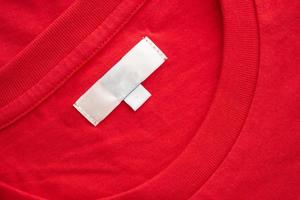 White blank clothing tag label on new red cotton shirt fabric texture background photo