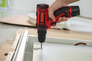 man assembling white table furniture at home using cordless screwdriver photo