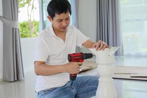 Asian man assembling white table furniture at home using cordless screwdriver photo