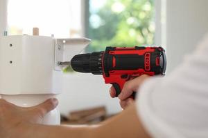 man assembling white table furniture at home using cordless screwdriver photo