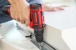 man assembling white table furniture at home using cordless screwdriver photo