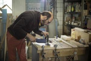 chico pule madera. el hombre trabaja en el taller de carpintería. procesamiento de madera foto