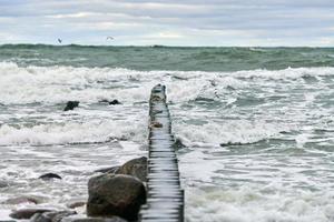 View of blue sea with foaming waves and wooden breakwaters photo